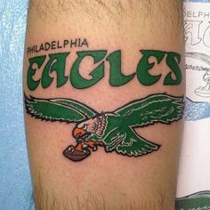 an eagle tattoo on the leg of a man with philadelphia eagles written in green ink