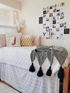 a white bed topped with lots of pillows next to a wall covered in pictures and photos