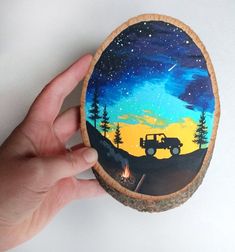 a hand holding a painted rock with a truck on it and the sky in the background