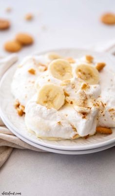 a white plate topped with whipped cream and banana slices next to cashews on a table