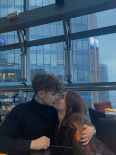 a man and woman kissing each other at a table in front of a large window