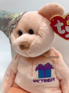 a pink teddy bear with a birthday hat on it's head and a gift tag attached to its ear