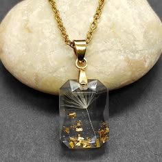 a necklace with a dandelion in it on a rock next to a stone