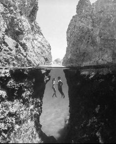 two people are swimming in the water near some rocks and cliffs, with one person diving into the water