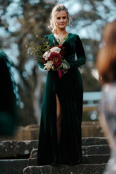 a woman in a long green dress is standing on some steps and holding a bouquet