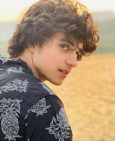 a young man with curly hair standing in front of a field