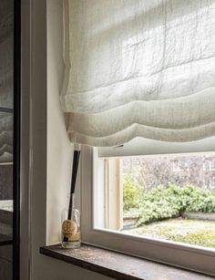 an open window with a white curtain in front of it and a vase next to the window sill