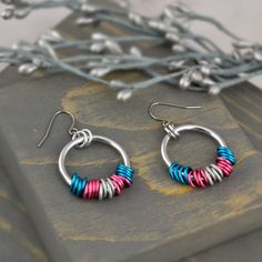 two pairs of colorful earrings sitting on top of a piece of wood next to branches