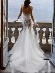 a woman in a white wedding dress looking out an open door at the ocean and mountains