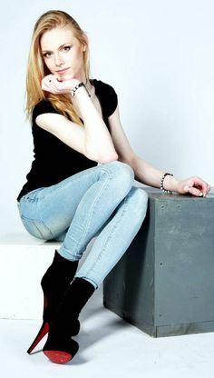 a woman in black shirt and jeans sitting on top of a metal box with her legs crossed