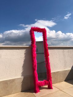 a pink mirror sitting on the side of a building next to a wall with clouds in the background