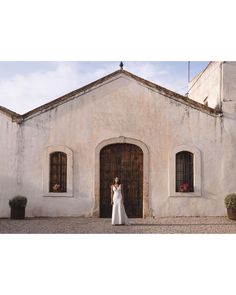 a woman standing in front of a white building wearing a wedding dress and looking at the camera