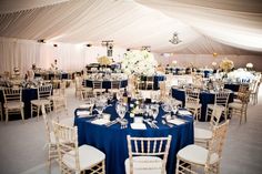 a large tent with tables and chairs set up for a formal function in blue linens