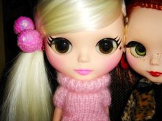 two dolls with blonde hair and green eyes, one wearing a pink sweater the other in a leopard print coat