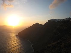 the sun is setting on top of a mountain overlooking the ocean and mountains in the distance