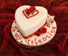 a white heart shaped cake with red roses on the bottom and writing happy valentine's day