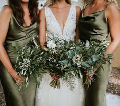 three beautiful women standing next to each other holding flowers and greenery in their hands