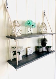 three shelves with plants and candles on them in a white walled room, one shelf is made out of wood and the other has rope