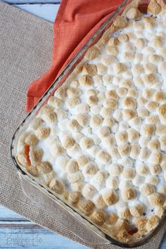 a casserole dish with marshmallows in it on a red cloth