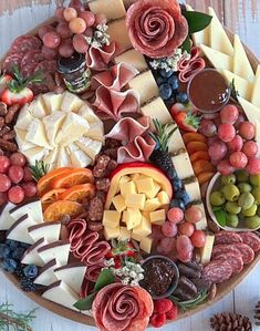 an assortment of cheeses, meats and fruit on a platter with pine cones