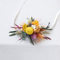 an arrangement of flowers and foliage on a white table cloth with a string attached to it