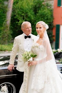 a bride and groom standing next to a black car