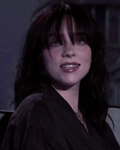 a close up of a person sitting in a chair with a purple wall behind her