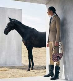 a woman is standing next to a horse and holding a purse in front of her