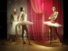 three mannequins dressed in white and pink tutus, with red curtains behind them