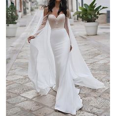 a woman in a white dress is walking down the street wearing a long veil over her head