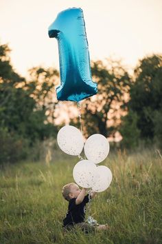 a young boy is holding balloons in the air while sitting on the grass and looking up