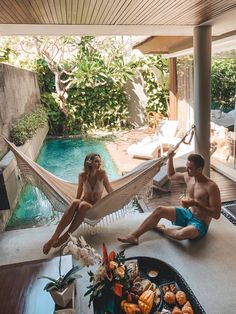 two people sitting in hammocks next to a pool with food on the table