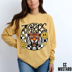 Roaring Tiger Long Sleeve Shirt - Checkered Background & Smiley Face - Comfy & Stylish Tee Stand out in the crowd with this unique long sleeve comfort colors t-shirt featuring a roaring tiger head on a checkered background. The design includes a yellow smiley face, stars, and a foam finger to show your team spirit at the game. Stay comfy and stylish with this eye-catching statement piece!   Add a playful touch to your wardrobe with this long sleeve comfort colors t-shirt showcasing a roaring tig Yellow Team Spirit T-shirt With Graphic Print, Yellow Casual Sublimation T-shirt With Graphic Print, Game Day Yellow Graphic Print Tops, Yellow Crew Neck Top For Team Spirit, Yellow School Spirit Graphic Print Top, Yellow College Top For Team Spirit, Custom Print Long Sleeve College T-shirt, Yellow Graphic Print Top For Game Day, Yellow Graphic Print Top For School Spirit