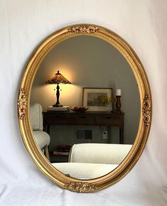 a round mirror sitting on top of a white bed next to a table with a lamp