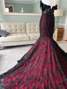 a red and black dress on display in front of a white couch with a mirror behind it