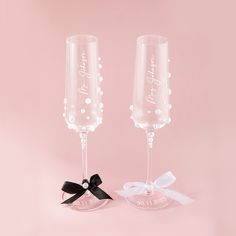 two wine glasses with black bows on them are sitting next to each other in front of a pink background