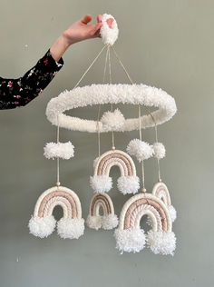 a hand is holding up a mobile with white pom - poms and rainbows