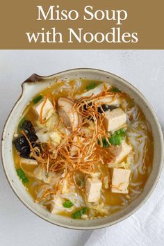 a bowl of miso soup with noodles and tofu in it on a white surface