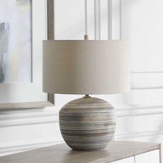 a table lamp sitting on top of a dresser next to a painting and framed pictures