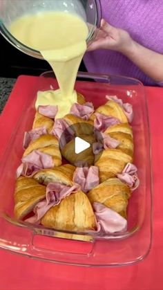 a person pouring sauce on top of pastries in a glass dish with red tray