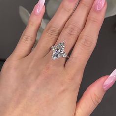 a woman's hand with pink and white manicured nails holding a diamond ring