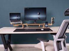 a computer desk with two monitors and a laptop on it in front of a blue wall