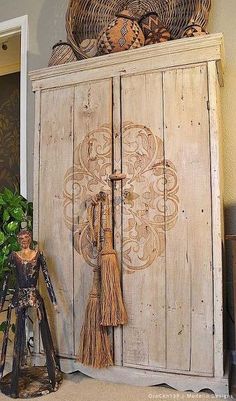 an old wooden cabinet with tassels and other items on top, sitting next to a potted plant