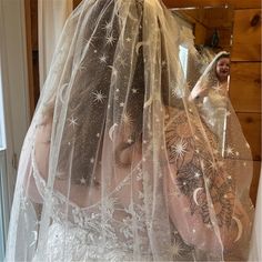 a woman in a wedding dress is looking at herself in the mirror while wearing a veil with stars on it