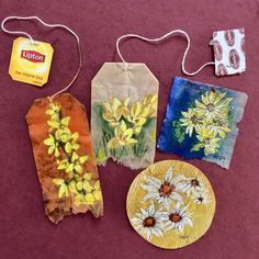 three tags with flowers on them are sitting on a red tablecloth next to other items