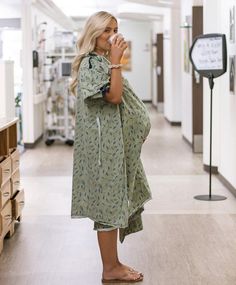 a woman standing in a hallway drinking from a cup with her hand on her hip