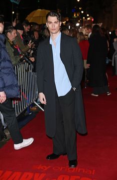 a man in a coat and tie standing on a red carpet