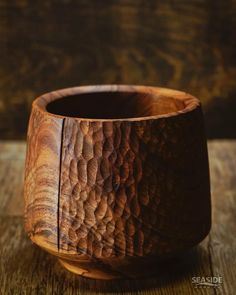 a wooden bowl sitting on top of a wooden table next to a black object in the background