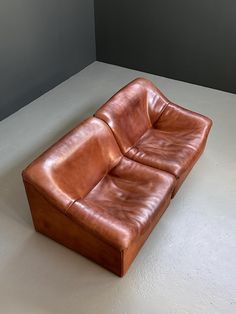 a brown leather couch sitting on top of a white floor next to a gray wall