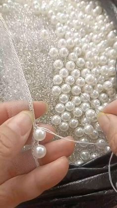 two hands are sewing pearls on a piece of netted fabric with scissors and thread